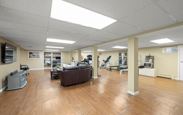 living area featuring baseboards, baseboard heating, a drop ceiling, and light wood-style flooring
