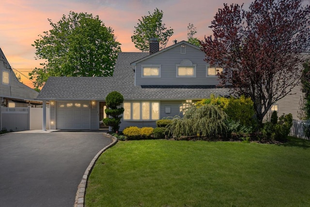 traditional-style home with fence, roof with shingles, an attached garage, aphalt driveway, and a yard