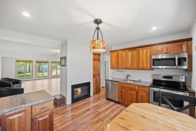 kitchen with appliances with stainless steel finishes, brown cabinets, a sink, open floor plan, and light wood-style flooring