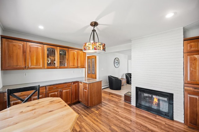 kitchen with brown cabinets, a fireplace, wood finished floors, a baseboard radiator, and glass insert cabinets