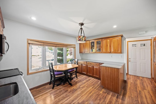 kitchen featuring brown cabinetry, stainless steel microwave, wood finished floors, and decorative light fixtures