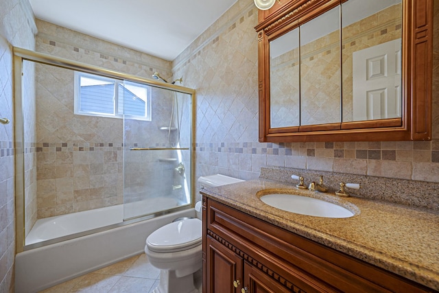 full bath with tile walls, tile patterned flooring, bath / shower combo with glass door, vanity, and toilet