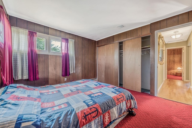 bedroom with a closet, carpet floors, wooden walls, and visible vents
