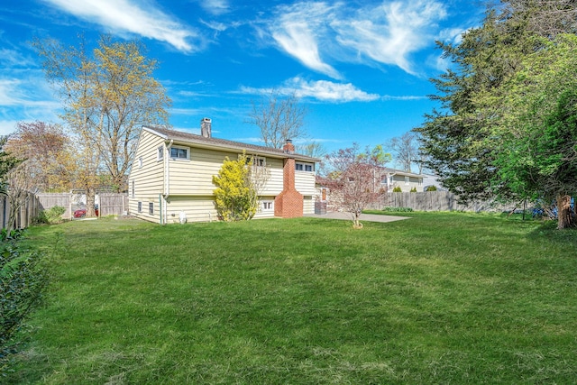 rear view of property with a fenced backyard, a chimney, and a yard