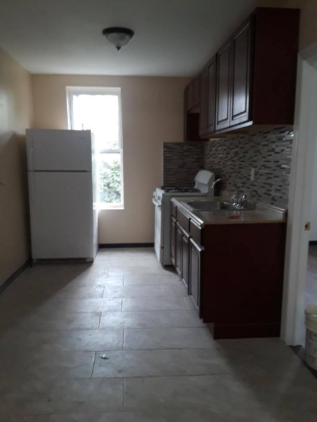 kitchen featuring freestanding refrigerator, decorative backsplash, dark brown cabinetry, gas range oven, and a sink