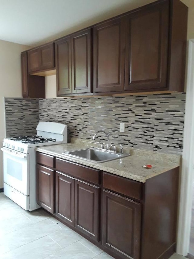 kitchen with a sink, decorative backsplash, light tile patterned floors, and white gas range