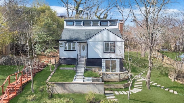 rear view of property with a chimney, a lawn, a deck, stairway, and a shingled roof
