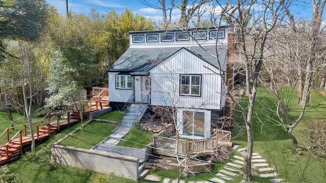 back of property with a wooden deck, a chimney, a shingled roof, a lawn, and stairway