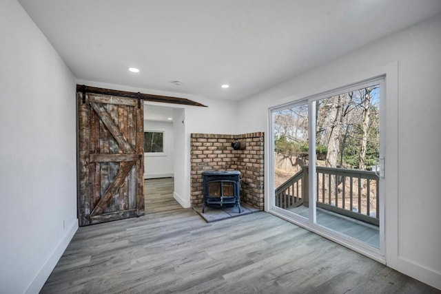 living room with a wood stove, wood finished floors, baseboards, recessed lighting, and a barn door