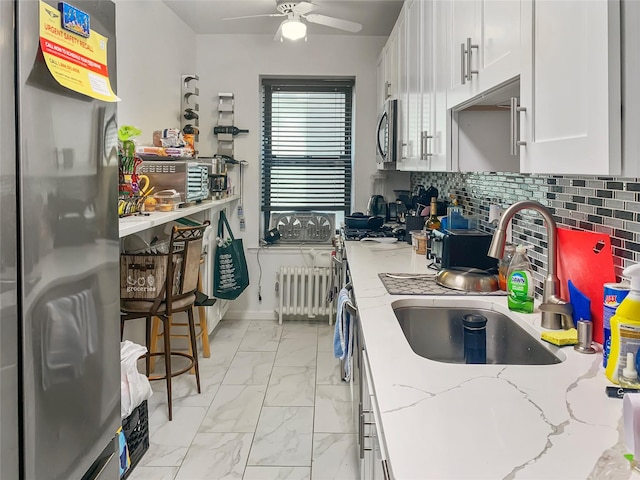 kitchen featuring a sink, white cabinets, marble finish floor, radiator heating unit, and stainless steel appliances