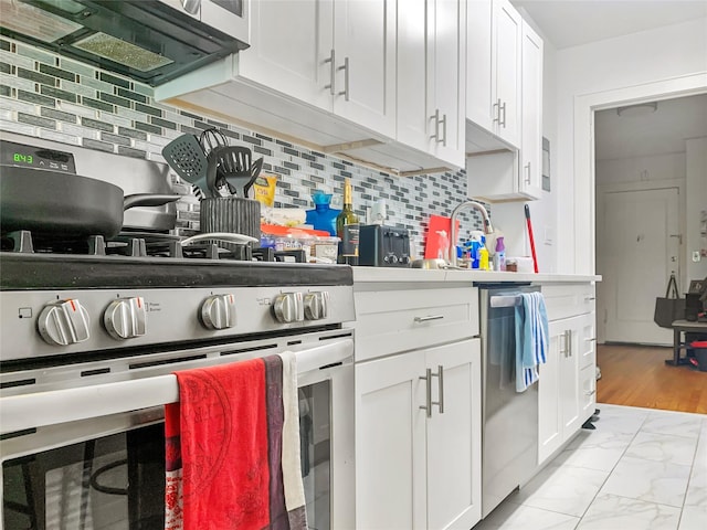 kitchen with tasteful backsplash, stainless steel appliances, white cabinetry, and marble finish floor