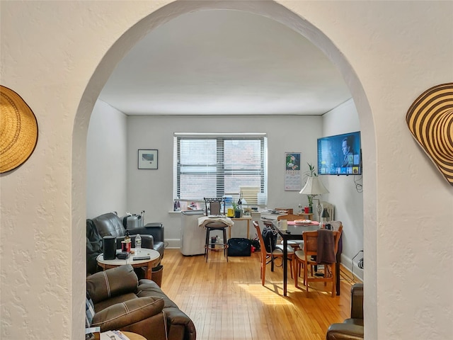 office space with arched walkways, light wood-style flooring, and a textured wall