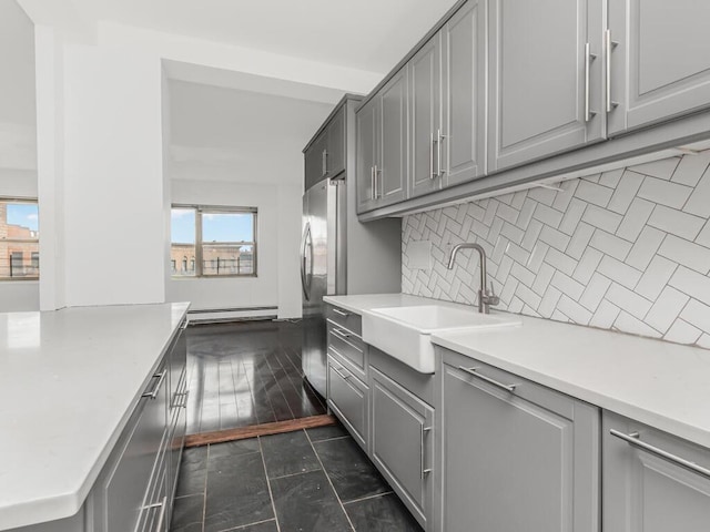 kitchen with a sink, light countertops, backsplash, a baseboard heating unit, and gray cabinetry