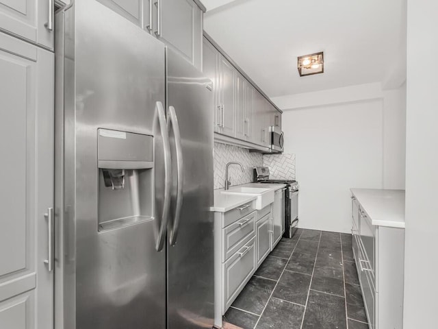 kitchen featuring tasteful backsplash, gray cabinetry, light countertops, a sink, and stainless steel appliances