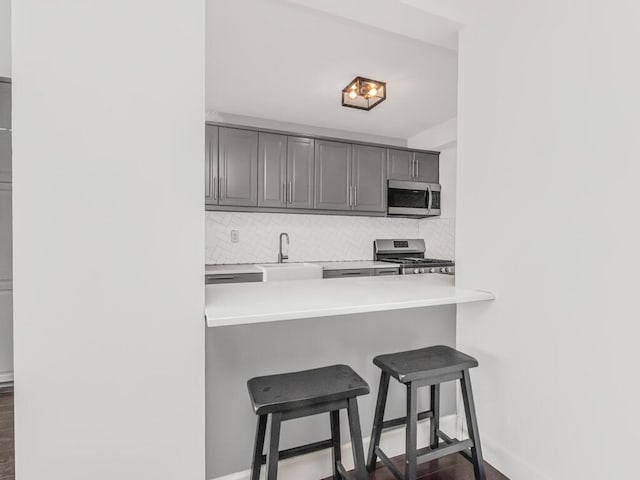 kitchen with appliances with stainless steel finishes, gray cabinets, baseboards, and a breakfast bar area