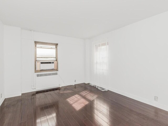 empty room with radiator heating unit, cooling unit, dark wood-style floors, and a healthy amount of sunlight