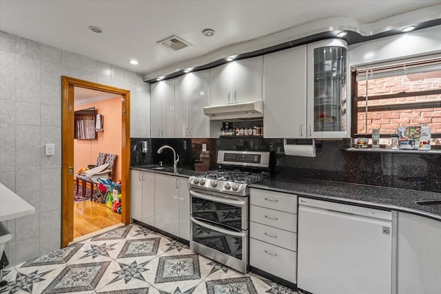 kitchen with white dishwasher, tile walls, under cabinet range hood, range with two ovens, and visible vents