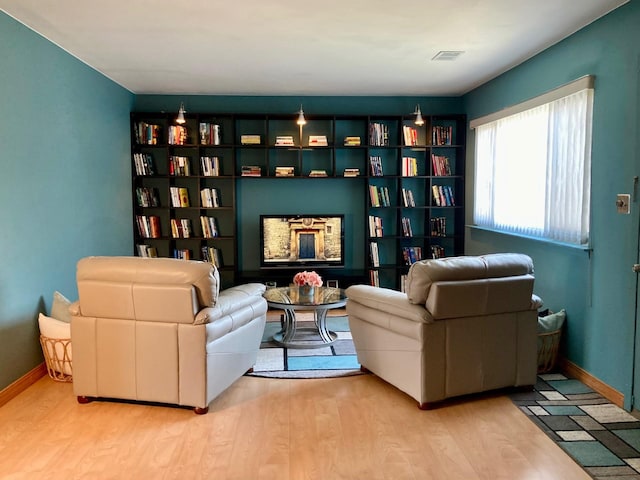 living area featuring baseboards, visible vents, wood finished floors, and a fireplace