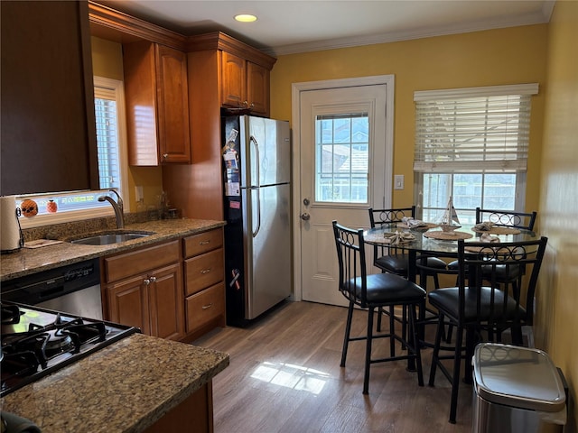 kitchen with brown cabinets, crown molding, a sink, stainless steel appliances, and wood finished floors