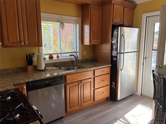 kitchen featuring brown cabinets, appliances with stainless steel finishes, a sink, and light wood-style floors