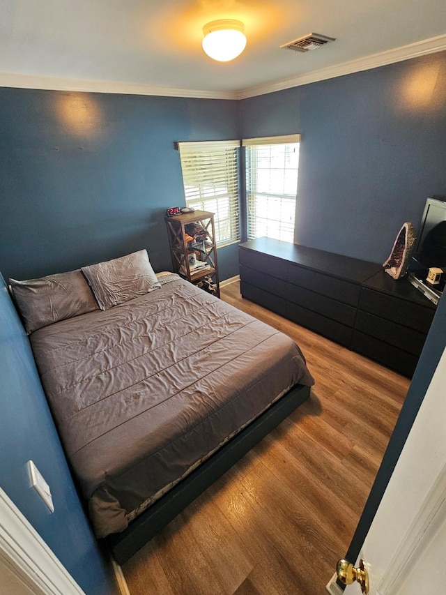 bedroom with crown molding, visible vents, and wood finished floors