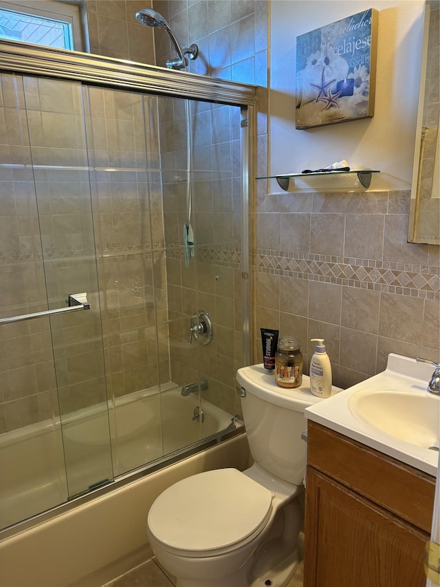 bathroom with shower / bath combination with glass door, vanity, toilet, and tile walls