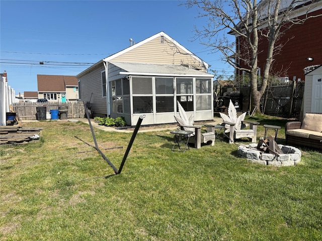 back of property featuring fence, a lawn, a sunroom, and a fire pit