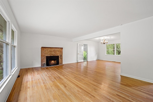 unfurnished living room featuring a chandelier, light wood-style floors, a fireplace, and baseboards