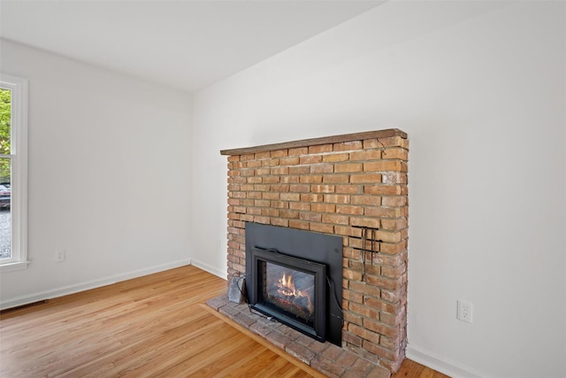 detailed view of wood finished floors, a brick fireplace, and baseboards