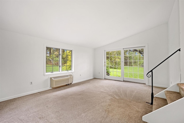 unfurnished living room featuring a wall mounted AC, healthy amount of natural light, vaulted ceiling, carpet flooring, and baseboards