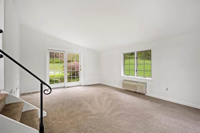 carpeted empty room featuring an AC wall unit, lofted ceiling, healthy amount of natural light, and baseboards
