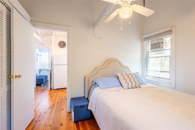 bedroom with ceiling fan, freestanding refrigerator, hardwood / wood-style flooring, and a wall unit AC