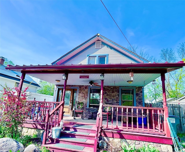 bungalow-style home with covered porch, fence, and stone siding