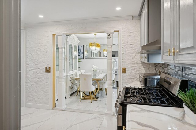 kitchen with wall chimney range hood, light stone countertops, stainless steel range with gas stovetop, a chandelier, and ornamental molding