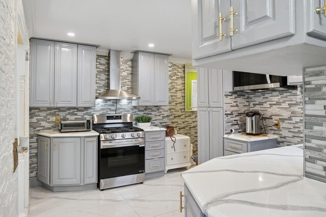 kitchen with gray cabinets, marble finish floor, wall chimney exhaust hood, gas range, and backsplash