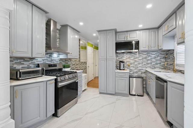 kitchen with a toaster, wall chimney range hood, gray cabinets, a sink, and stainless steel appliances