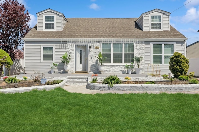 cape cod home featuring roof with shingles, stone siding, and a front yard