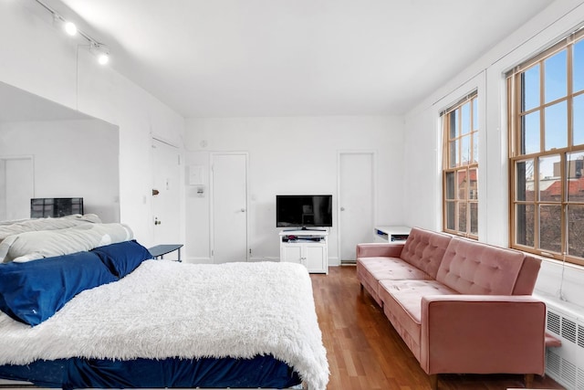 bedroom with track lighting, wood finished floors, and radiator heating unit