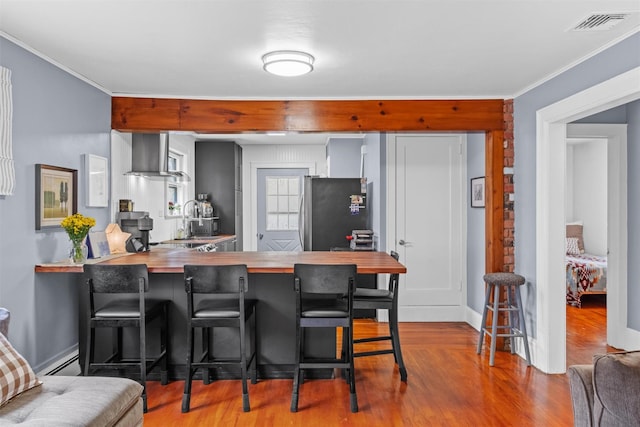 kitchen with butcher block countertops, a peninsula, wood finished floors, freestanding refrigerator, and ventilation hood