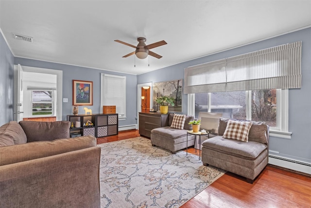living area featuring ceiling fan, plenty of natural light, visible vents, and a baseboard heating unit
