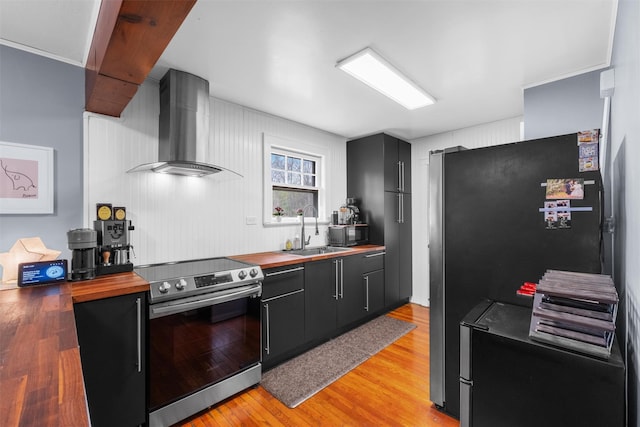 kitchen with butcher block countertops, light wood finished floors, a sink, wall chimney exhaust hood, and electric range