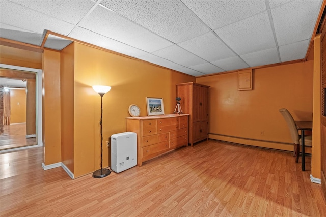 basement with light wood-style floors, a drop ceiling, baseboards, and a baseboard heating unit