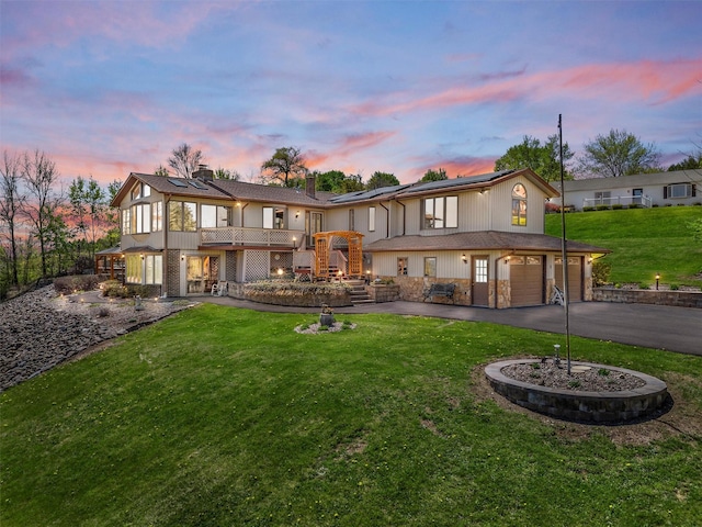 back of house at dusk featuring an attached garage, stairway, solar panels, a lawn, and driveway