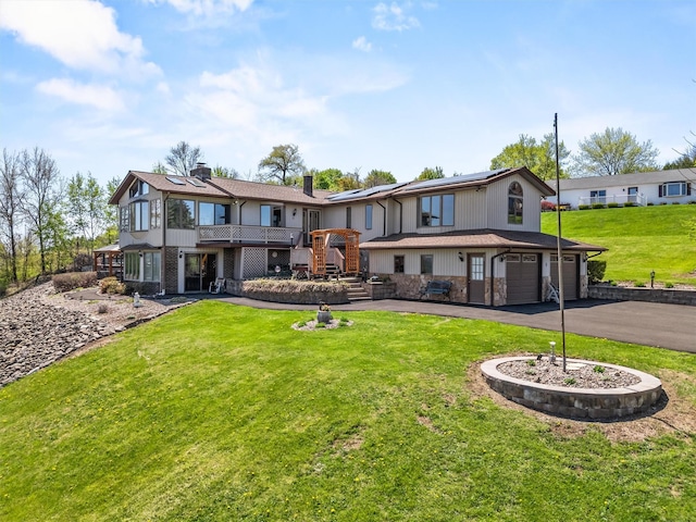 back of property with a garage, stairway, solar panels, a lawn, and driveway