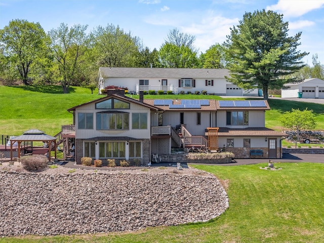 back of property with a gazebo, roof mounted solar panels, a lawn, and stairway