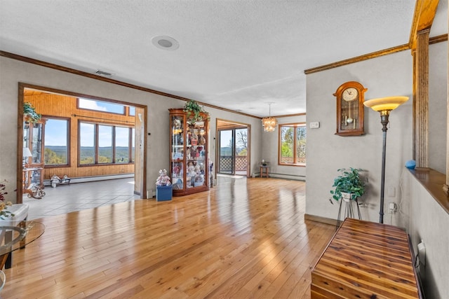 interior space featuring a textured ceiling, visible vents, baseboard heating, light wood finished floors, and ornamental molding