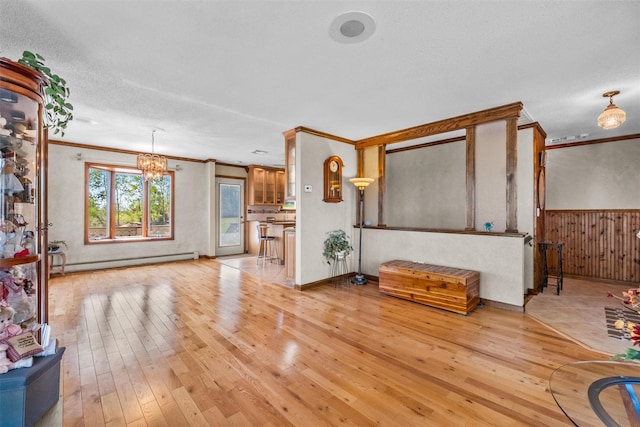 unfurnished living room with an inviting chandelier, ornamental molding, baseboard heating, and light wood-style flooring