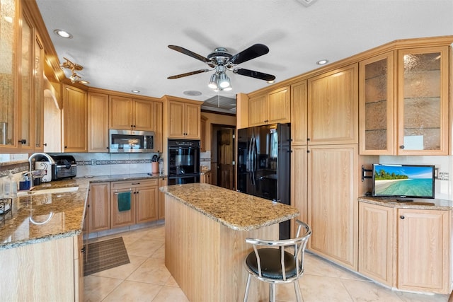 kitchen with light stone countertops, a center island, a ceiling fan, light tile patterned floors, and black appliances