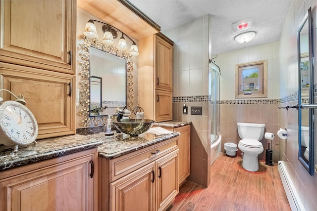 full bath with wood finished floors, toilet, tile walls, a textured ceiling, and a baseboard heating unit