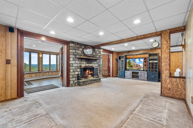 unfurnished living room featuring wood walls, a fireplace, a drop ceiling, a baseboard heating unit, and carpet flooring